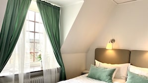 A hotel room with a bed, pillows, a nightstand, a lamp, and a window with curtains. - Tokeryds Herrgård (Jonkoping)