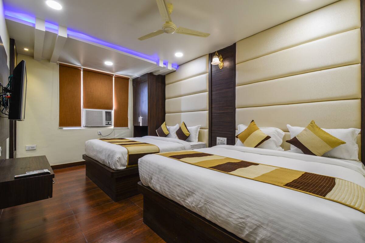 Habitación de hotel con dos camas, ventilador de techo, luces empotradas, televisor y aire acondicionado.