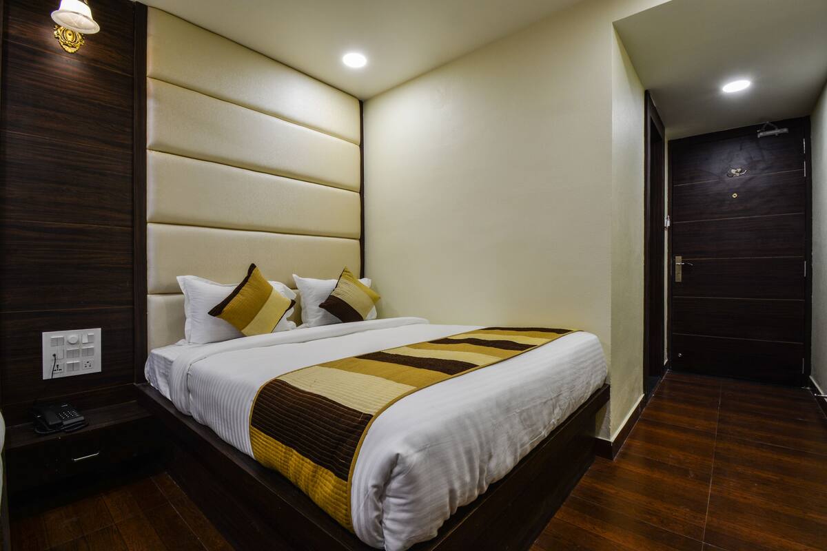 Una habitación de hotel con una cama grande, una mesita de noche con un teléfono y una puerta a la derecha.