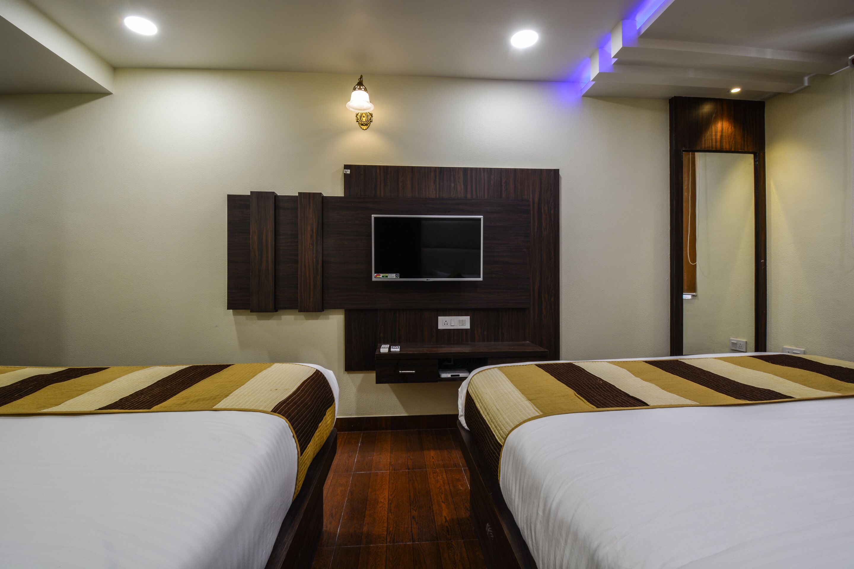 Habitación de hotel con dos camas, un televisor de pantalla plana montado en la pared y un espejo.