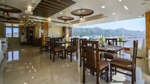 A modern dining area with a view of mountains, featuring a polished floor, wooden chairs, and contemporary ceiling design. - Hotel Atlantica Ajmer (Ajmer)