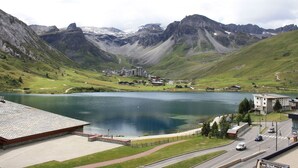 A lakeside hotel with a view of mountains, a parking area, and a road.