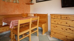 A cozy room with a wooden table and bench, a wooden dresser, a wall-mounted TV, and a framed picture.