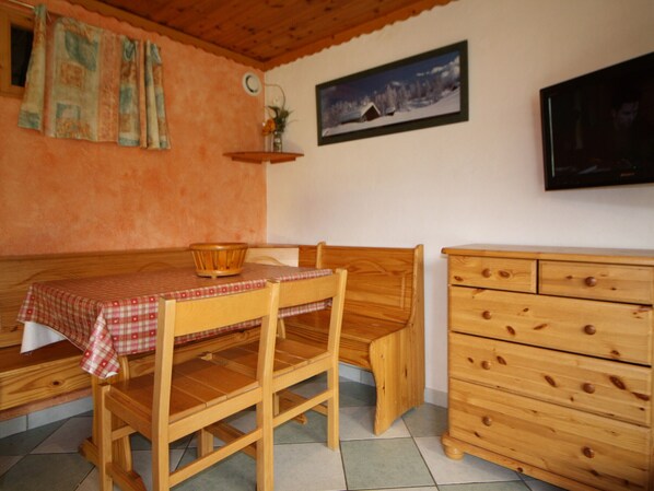 Ein gemütliches Zimmer mit Holztisch und Bank, einem Holzschrank, einem an der Wand befestigten Fernseher und einem gerahmten Bild.