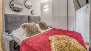 Ein modernes Schlafzimmer mit einem grau gepolsterten Kopfteil, einer roten Decke und zwei flauschigen Kissen.