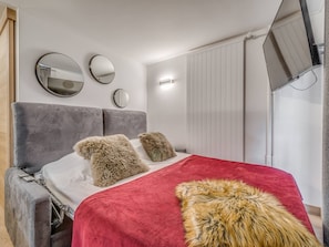 Une chambre moderne avec une tête de lit rembourrée de couleur grise, une couverture rouge et deux coussins moelleux.