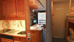 A compact kitchen with wooden cabinets, a sink, and a dining area with a table and chairs. - Large studio for 4 ppl. with balcony and lake view in Tignes (Tignes)