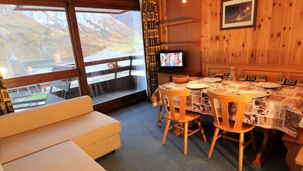 A cozy room with a wooden dining table set for four, a television, and a large window with a view of a mountainous landscape. - Large studio for 4 ppl. with balcony and lake view in Tignes (Tignes)