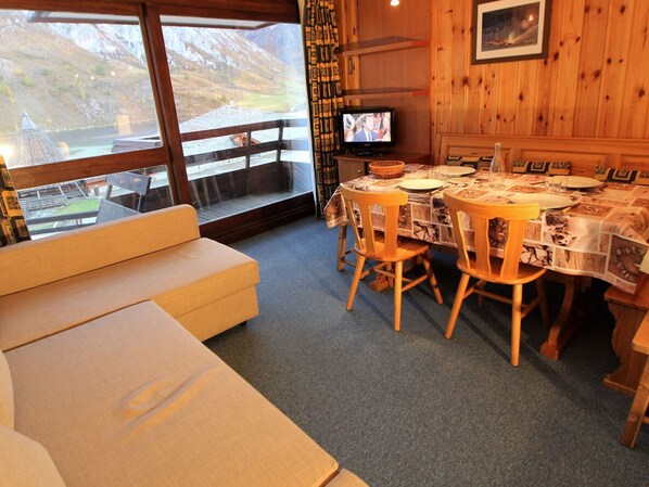 A cozy room with a wooden dining table set for four, a television, and a large window with a view of a mountainous landscape. - Large studio for 4 ppl. with balcony and lake view in Tignes (Tignes)