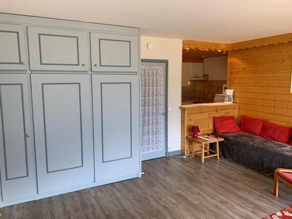 Ein Zimmer mit einem grauen Wäscheschrank, einer hölzernen Bank mit roten Kissen und einem kleinen Tisch mit einer Lampe.