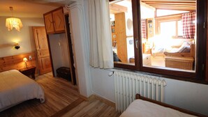 A cozy room with two beds, wooden floors, a radiator, and a window with curtains. - Traditional Chalet in Tignes - 3 rooms, 6 people, WiFi included (Tignes)