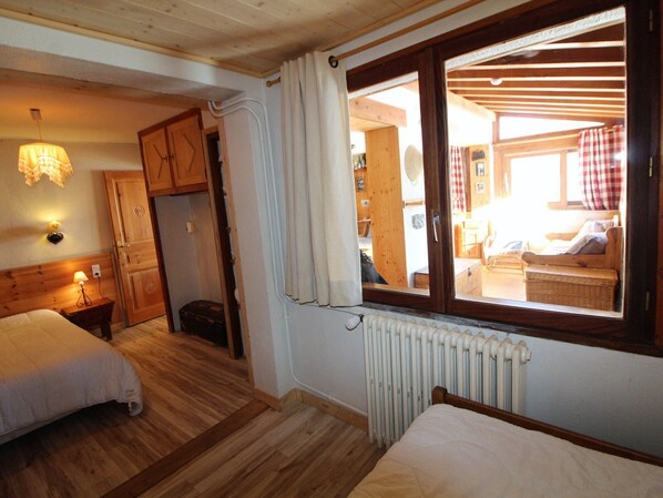 A cozy room with two beds, wooden floors, a radiator, and a window with curtains.