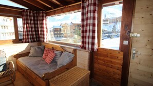 A cozy wooden cabin room with a bed, a wicker basket, and a view of buildings outside. - Traditional Chalet in Tignes - 3 rooms, 6 people, WiFi included (Tignes)