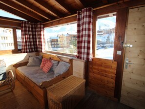 A cozy wooden cabin room with a bed, a wicker basket, and a view of buildings outside. - Traditional Chalet in Tignes - 3 rooms, 6 people, WiFi included (Tignes)