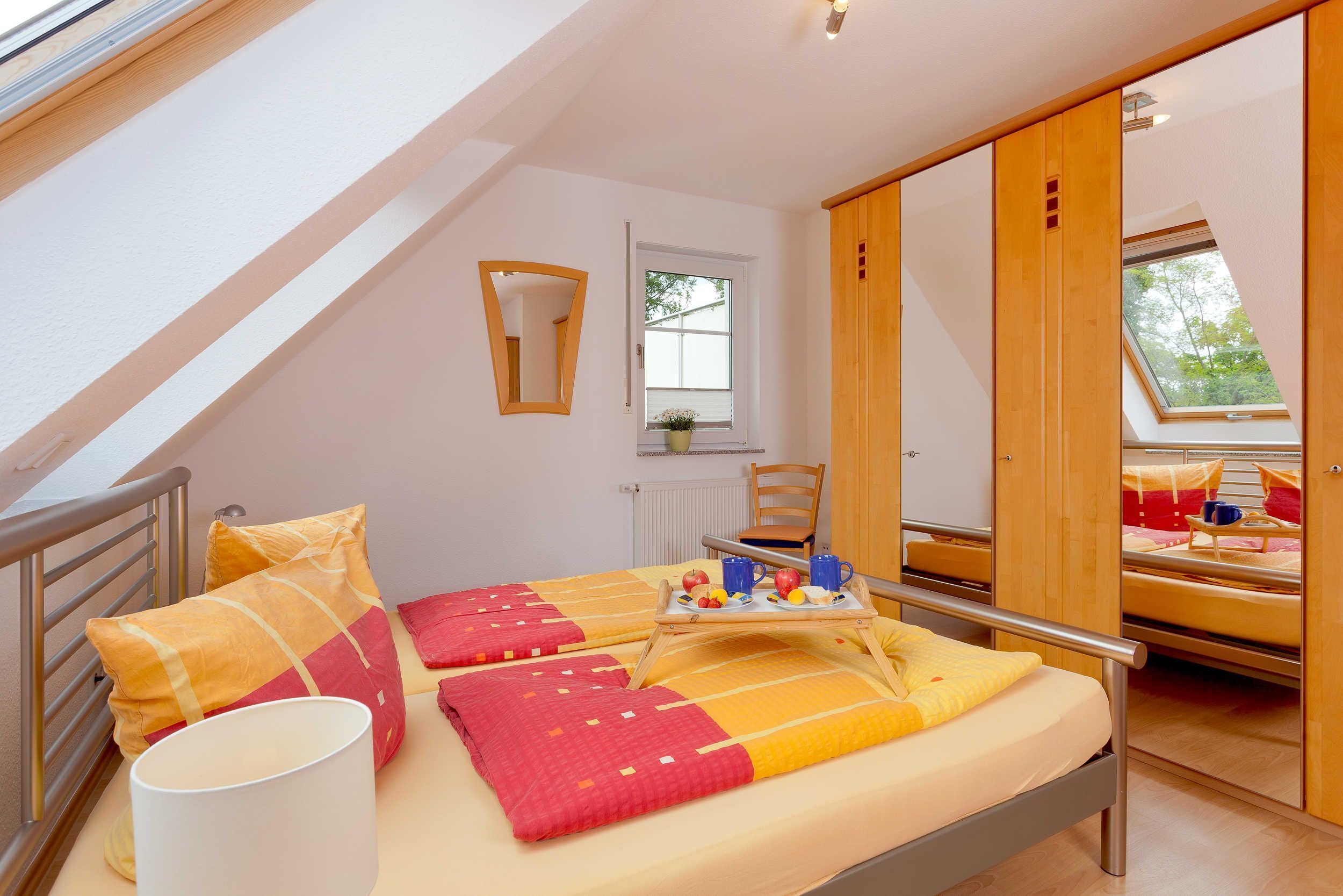 A bedroom with a bed, a bedside table with a tray of fruit, a chair, and a window.