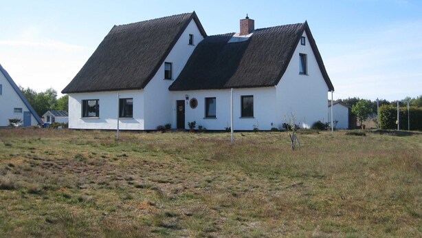 Una casa blanca de dos pisos con techo negro, chimenea y un pequeño jardín.