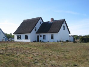 Una casa blanca de dos pisos con techo negro, chimenea y un pequeño jardín.