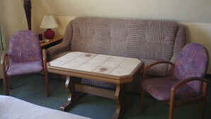 Una habitación con sofá, dos sillones, una mesita, lámpara y un florero.