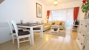 A modern living room with a dining table, chairs, a sofa, and a coffee table. - App Kapitänsstube, Germany (Sylt)