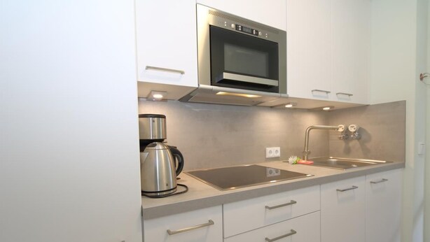 A modern kitchen with a built-in microwave, a kettle, and a sink. - App Kapitänsstube, Germany (Sylt)