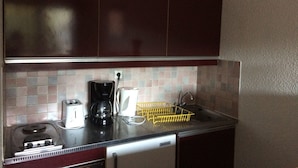 A compact kitchenette with a toaster, coffee maker, and a yellow dish rack.