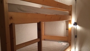 A bunk bed with a wooden frame and a mattress. There is a wall-mounted light fixture on the right side.