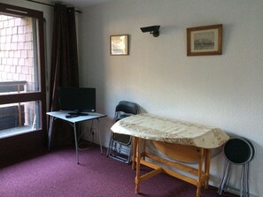 Een kamer met een bureau, een televisie, een bed en twee stoelen.