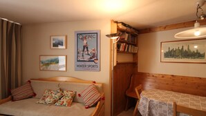 A cozy room with a wooden bed, a small table with a tablecloth, a bookshelf, and a poster on the wall. - Spacious 3-room family apt - 2 bathrooms - Lake view balcony (Tignes)