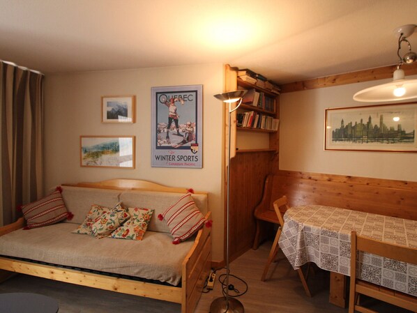 Une pièce chaleureuse avec un lit en bois, une petite table recouverte d’une nappe, une bibliothèque et une affiche accrochée au mur.