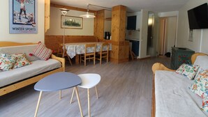 A cozy living room with a sofa, a small table, and a kitchen area in the background. - Spacious 3-room family apt - 2 bathrooms - Lake view balcony (Tignes)