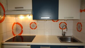 A kitchen with white cabinets, a blue upper cabinet, a stainless steel sink, and decorative orange and white tiles. - Spacious 3-room family apt - 2 bathrooms - Lake view balcony (Tignes)