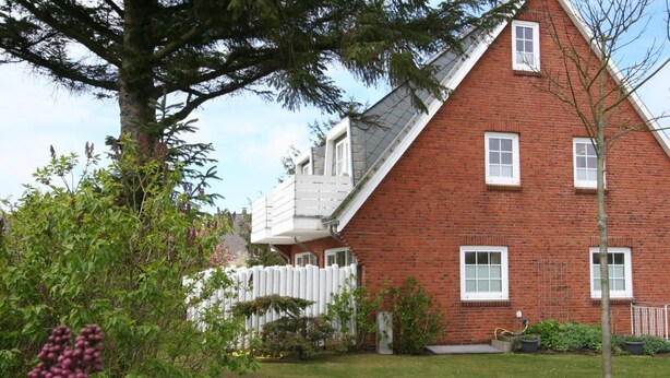 A red brick building with a white balcony, surrounded by greenery and a white fence. - Spieker Wenningstedt (Wenningstedt-Braderup (Sylt))