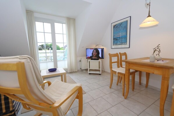 Une pièce comprenant une table à manger, des chaises, un téléviseur et une fenêtre avec des rideaux.