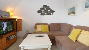 A living room with a television, a white coffee table, a brown sofa, and yellow cushions. - Syltnest Munkmarsch, Germany (Sylt-Ost)
