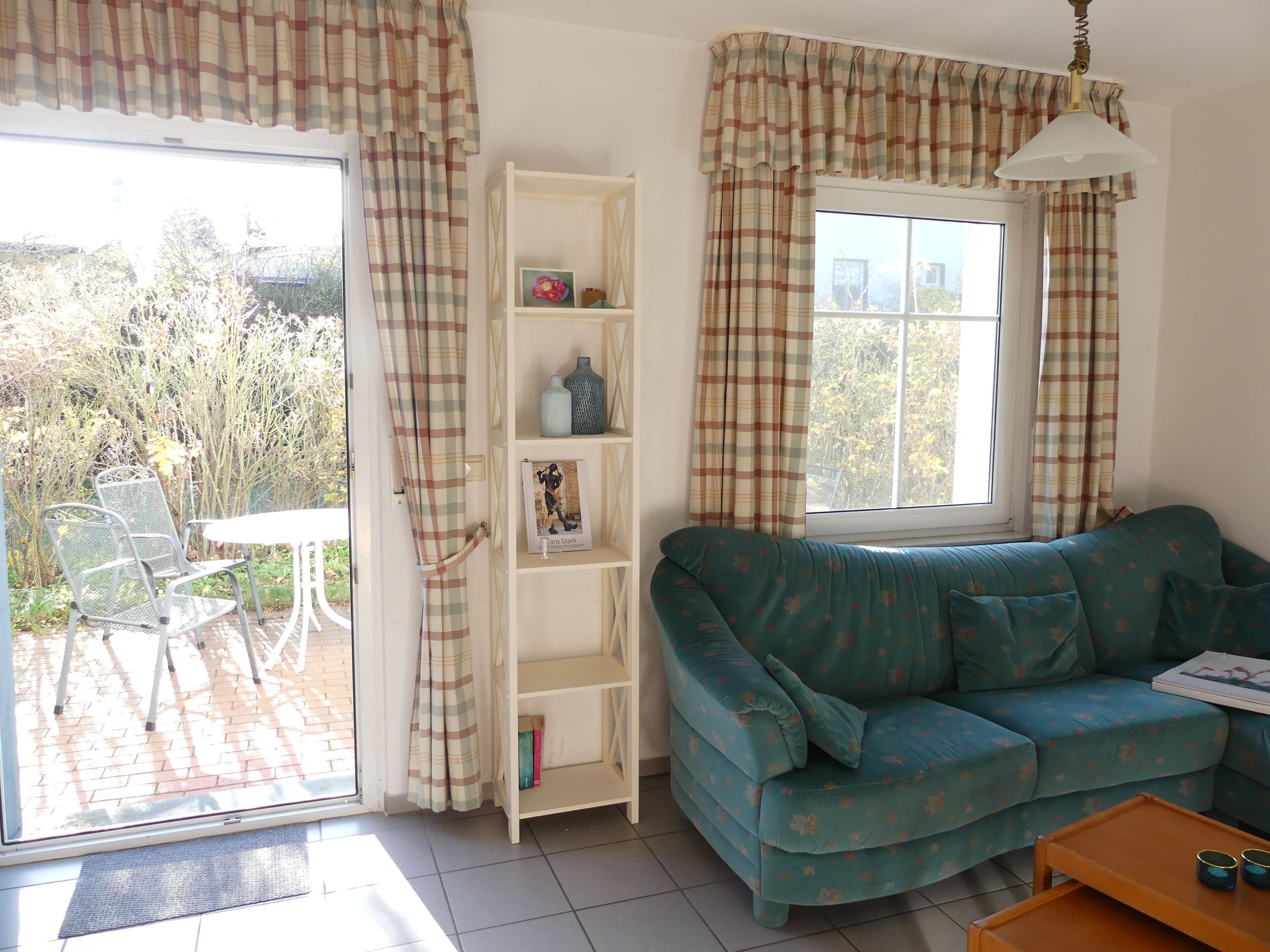 Ein Wohnzimmer mit einer Couch, einem kleinen Tisch, einem Bücherregal und einem Fenster mit Vorhängen.