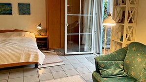 A bedroom with a bed, a nightstand, a green sofa, a wardrobe, and a sliding glass door leading to a balcony.