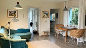 A living room with a sofa, a dining table, chairs, a lamp, and artwork on the walls.