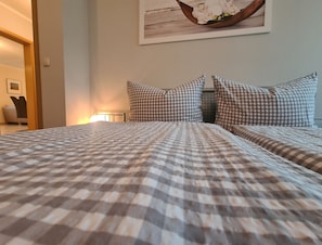 Ein Bett mit kariertem Überwurf, einem Kopfteil und einem an der Wand hängenden Bild.