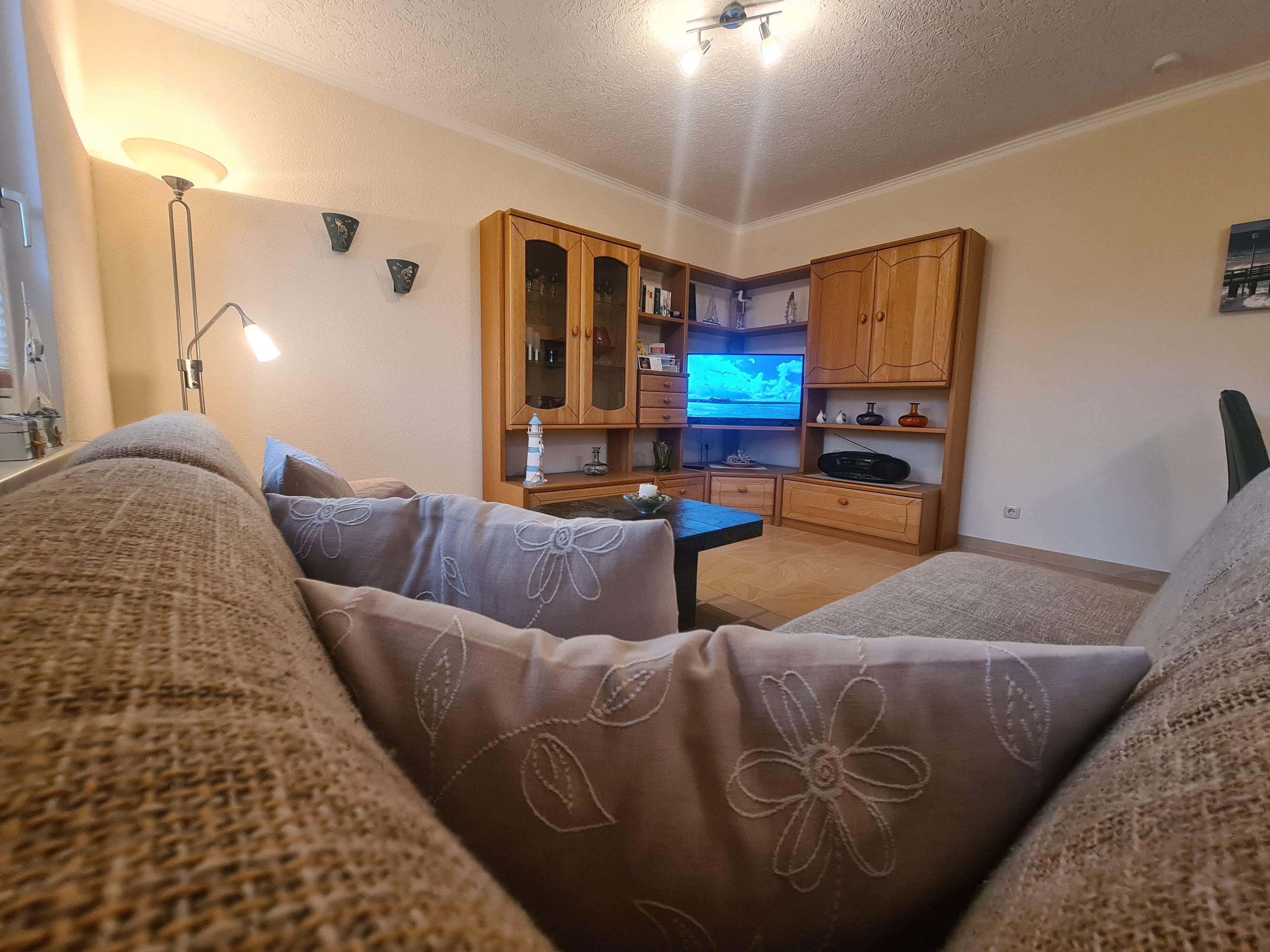 Ein gemütliches Wohnzimmer mit einer Couch, einem Fernseher, Holzschränken und einer Lampe.