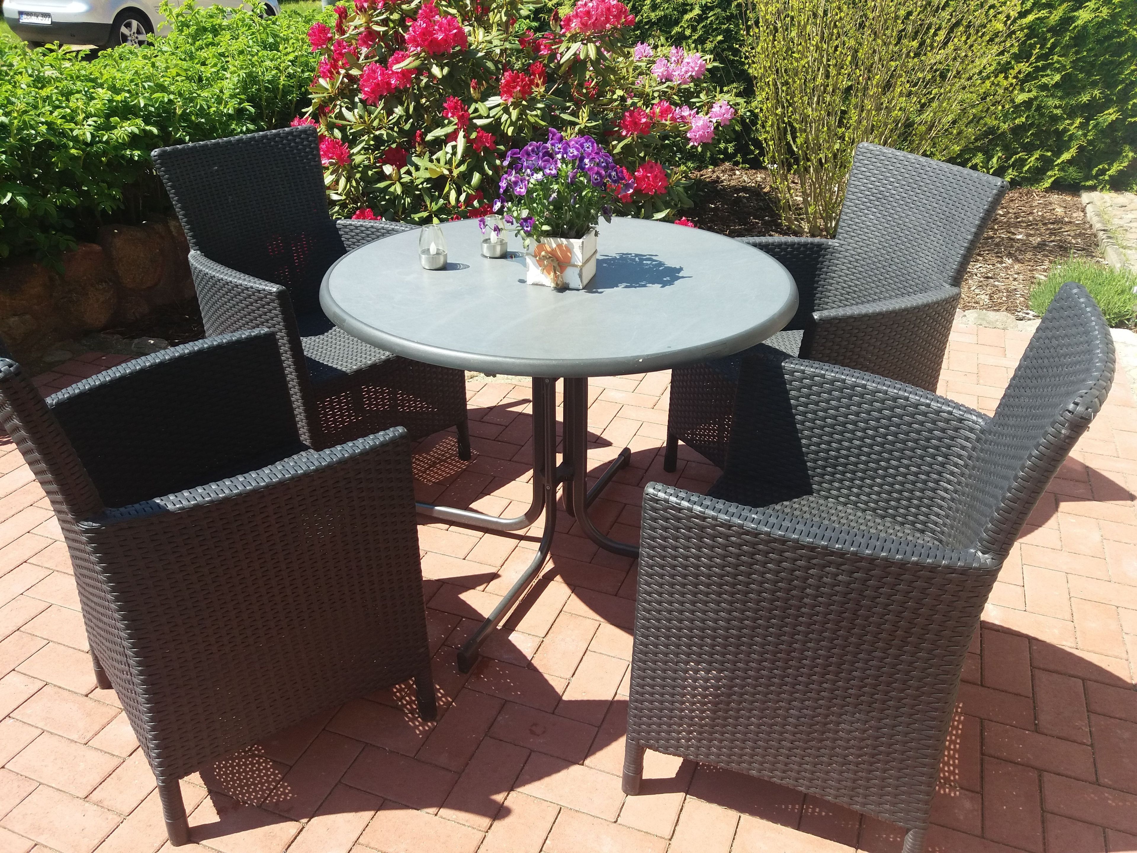 Ein runder Gartentisch mit Korbstühlen, umgeben von einem Garten mit verschiedenen Blumen.