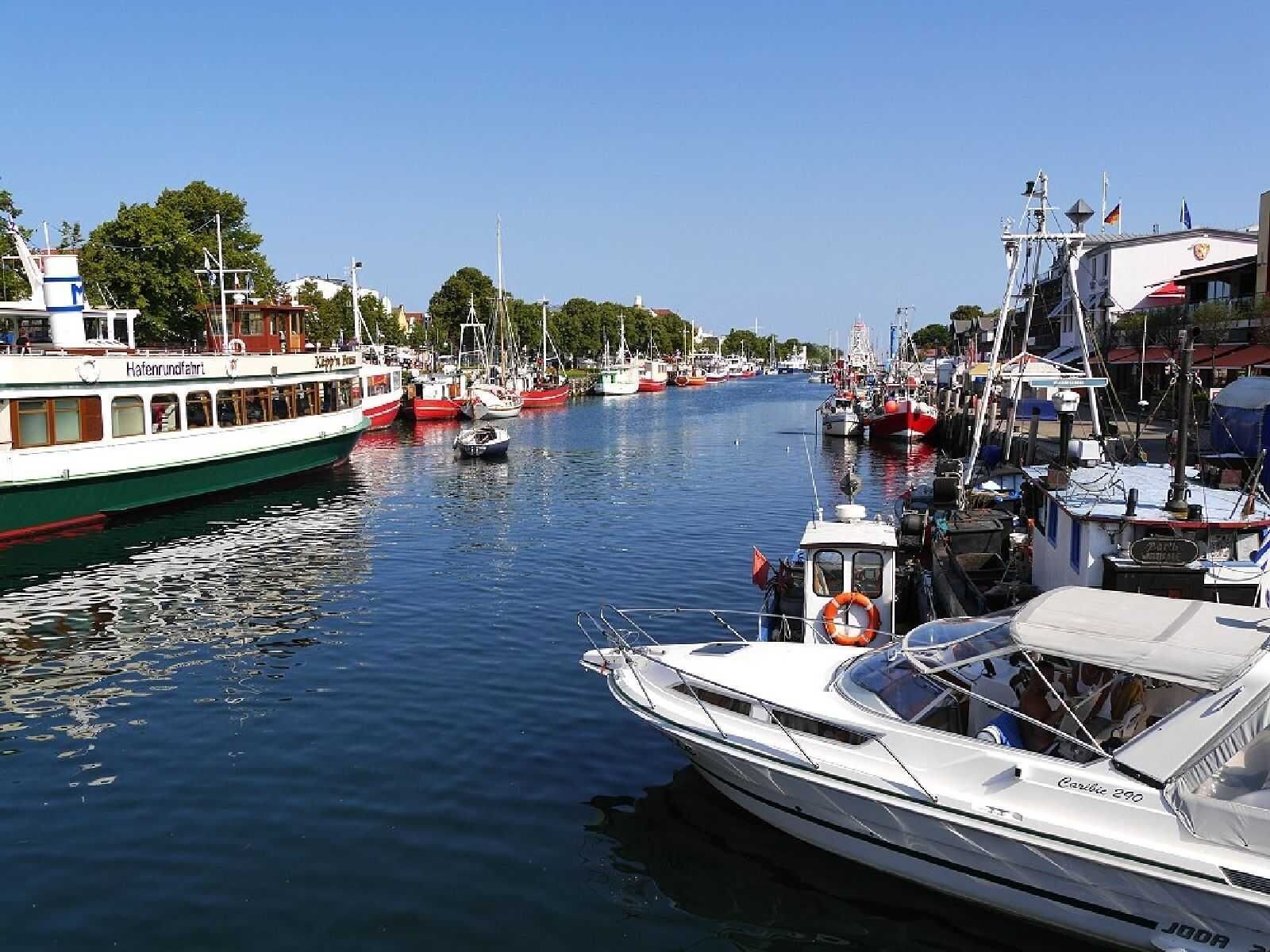 Una marina amb diverses embarcacions amarrades, una embarcació blanca amb la inscripció 'Hafenrundfahrt' al costat, i una embarcació anomenada 'Caroline 290'.