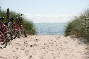 Ein Sandweg am Strand mit abgestellten Fahrrädern links, der zum Meer führt.