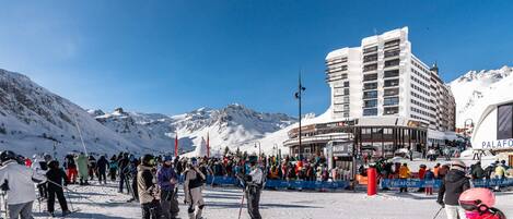 Une station de ski avec un grand bâtiment, probablement un hôtel ou un centre de villégiature, et une foule de personnes sur la neige.