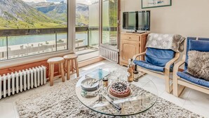 A modern living room with a large window offering a scenic mountain view, a cozy seating area with a blue sofa, and a glass coffee table with a cake.