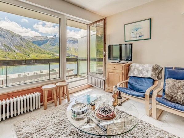 A modern living room with a large window offering a scenic mountain view, a cozy seating area with a blue sofa, and a glass coffee table with a cake. - 3-room apartment for 8 people in Tignes, near lake and slopes (Tignes)