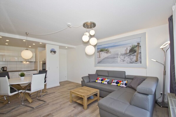 A modern living room with a grey sofa, a wooden coffee table, and a dining area with white chairs and a small table.