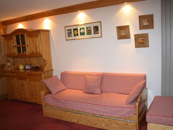 A cozy room with a wooden cabinet, a red and white patterned sofa, and framed pictures on the wall.