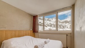 Un dormitorio con cabecera de madera, un ventanal con vistas a la montaña y una toalla enrollada sobre la cama.