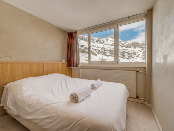 Une chambre avec une tête de lit en bois, une grande fenêtre donnant sur les montagnes et une serviette enroulée posée sur le lit.
