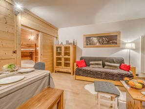Una habitación acogedora con literas, una zona de comedor con una mesa preparada para dos personas, un sofá con cojines, un armario y un cuadro en la pared.